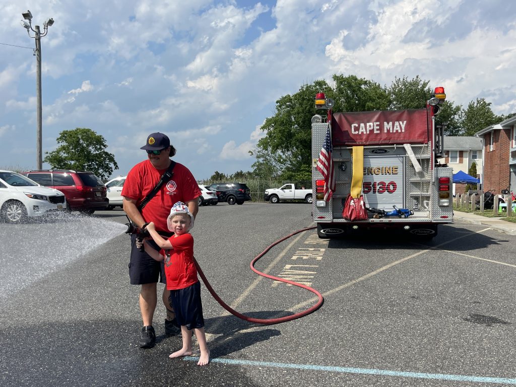 little boy and cape may firefighter spraying hose together
