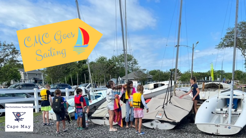 a group of children by sailboats with "CMC goes sailing" as the banner
