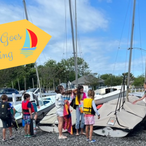 a group of children by sailboats with "CMC goes sailing" as the banner