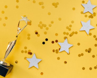 yellow background with a trophy in the foreground and stars with glitter scattered on the floor